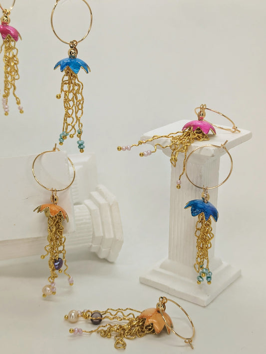 A collection of jelly fish inspired earrings, displayed on white columns, some jelly fish earrings are hanging in mid air. The jelly fish are various colours including blue, orange and pink with a cascade of gold plated tentacles with freshwater pearls