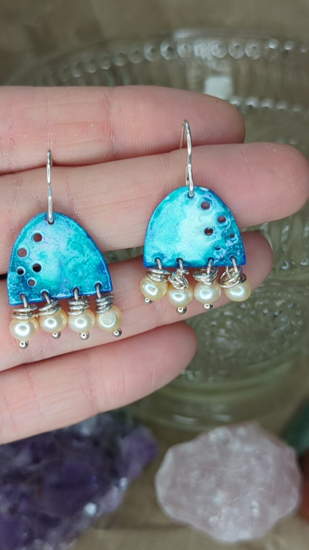 Video of blue enamel earring adorned with apricot freshwater pearls, placed on a hand, the earrings are moving to show all the blue colours