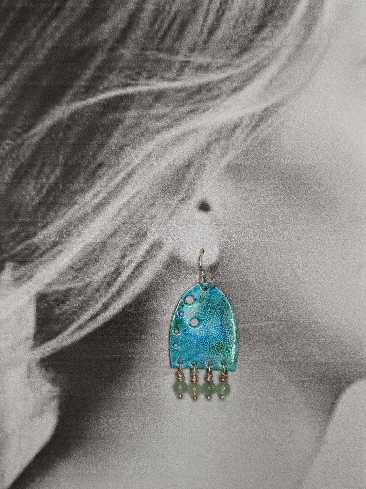 Black and white image of a model wearing turquoise earrings with green aventurine beads.