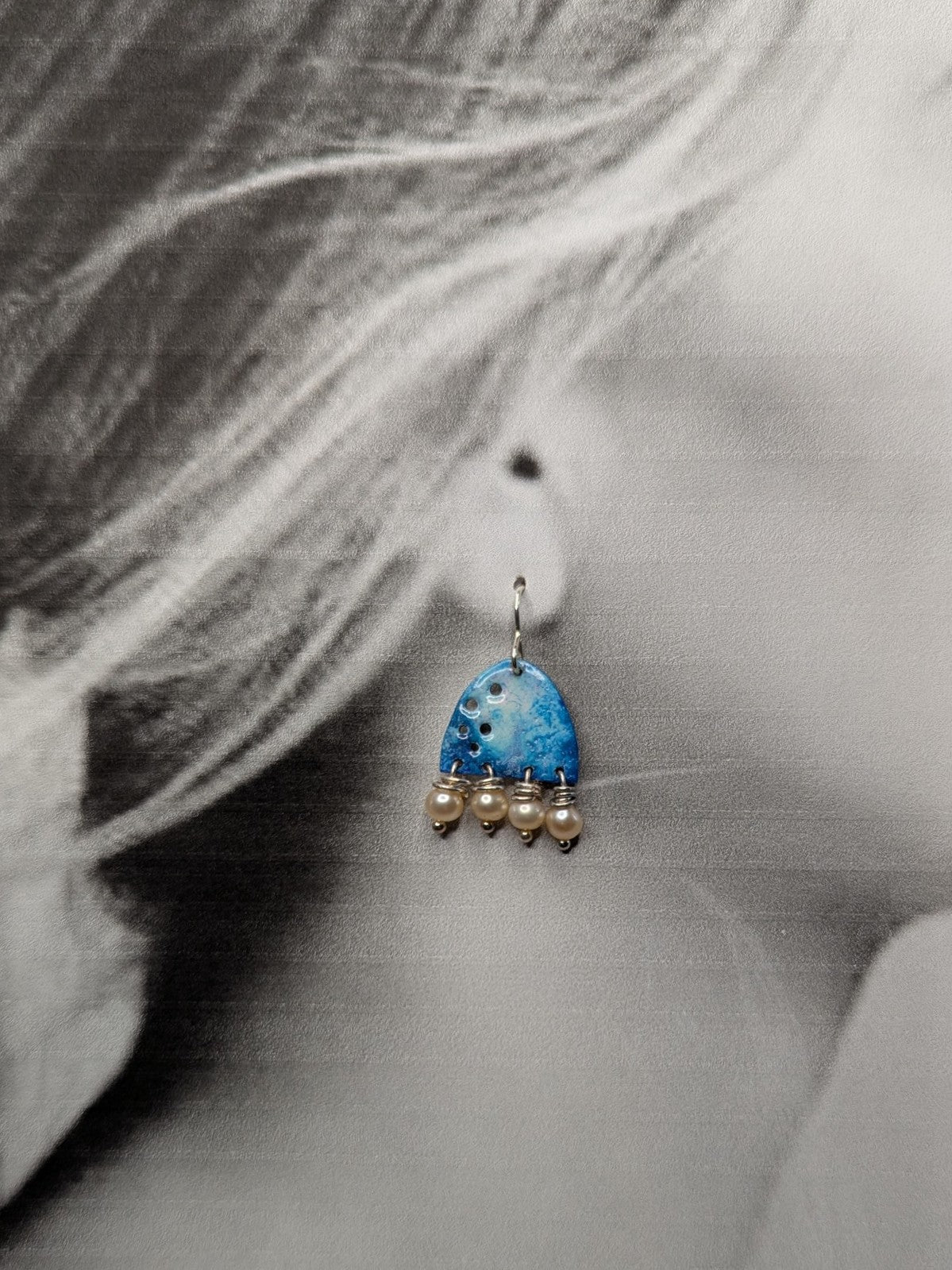 Black and white image of a model wearing blue enamel earrings adorned with freshwater pearls