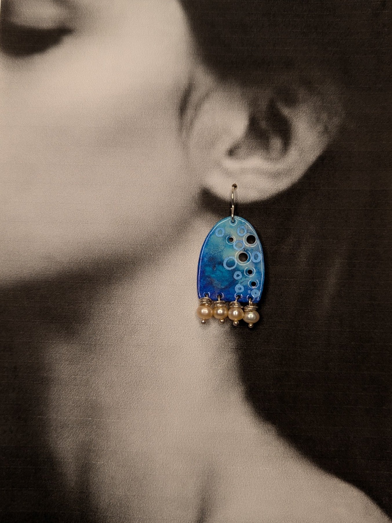 Black and white image of a model wearing blue enamel earrings adorned with freshwater pearls