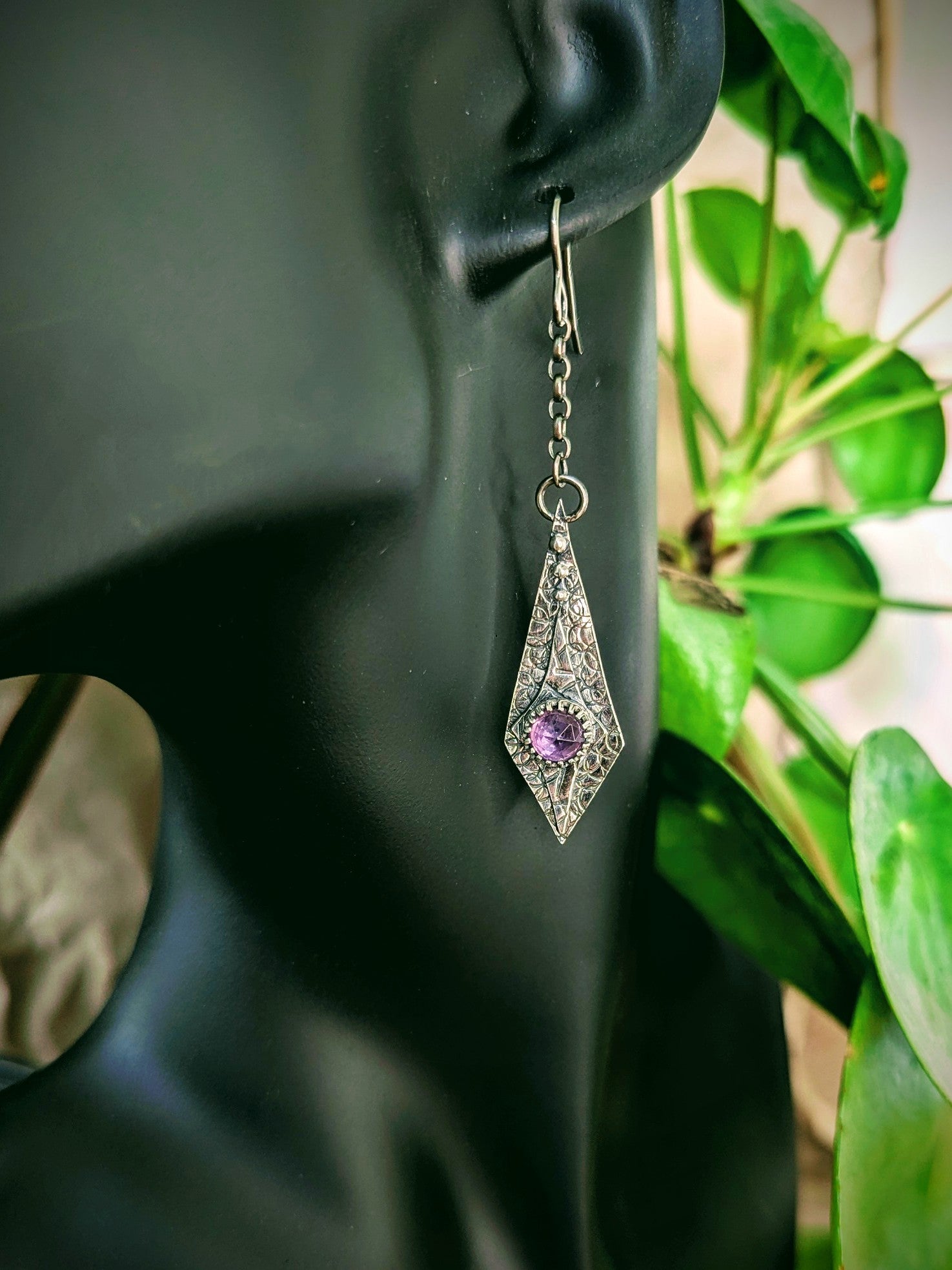 Maiden Earrings displayed on a black mannequin's ear, with lush green plants softly blurred in the background, showcasing the jewellery’s vintage charm against a natural backdrop.