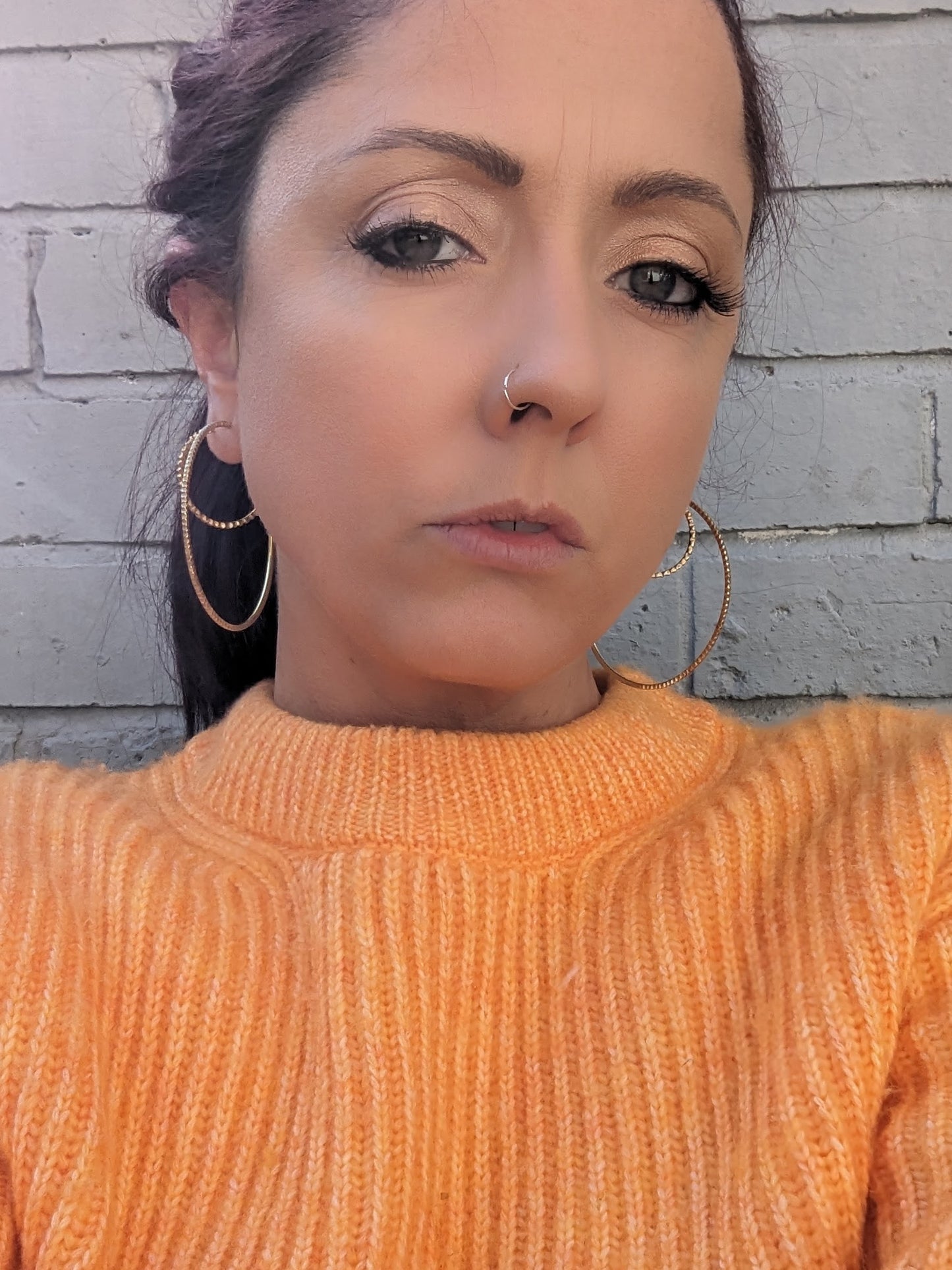 "Model wearing an orange jumper showcasing large gold brass goddess hoops."