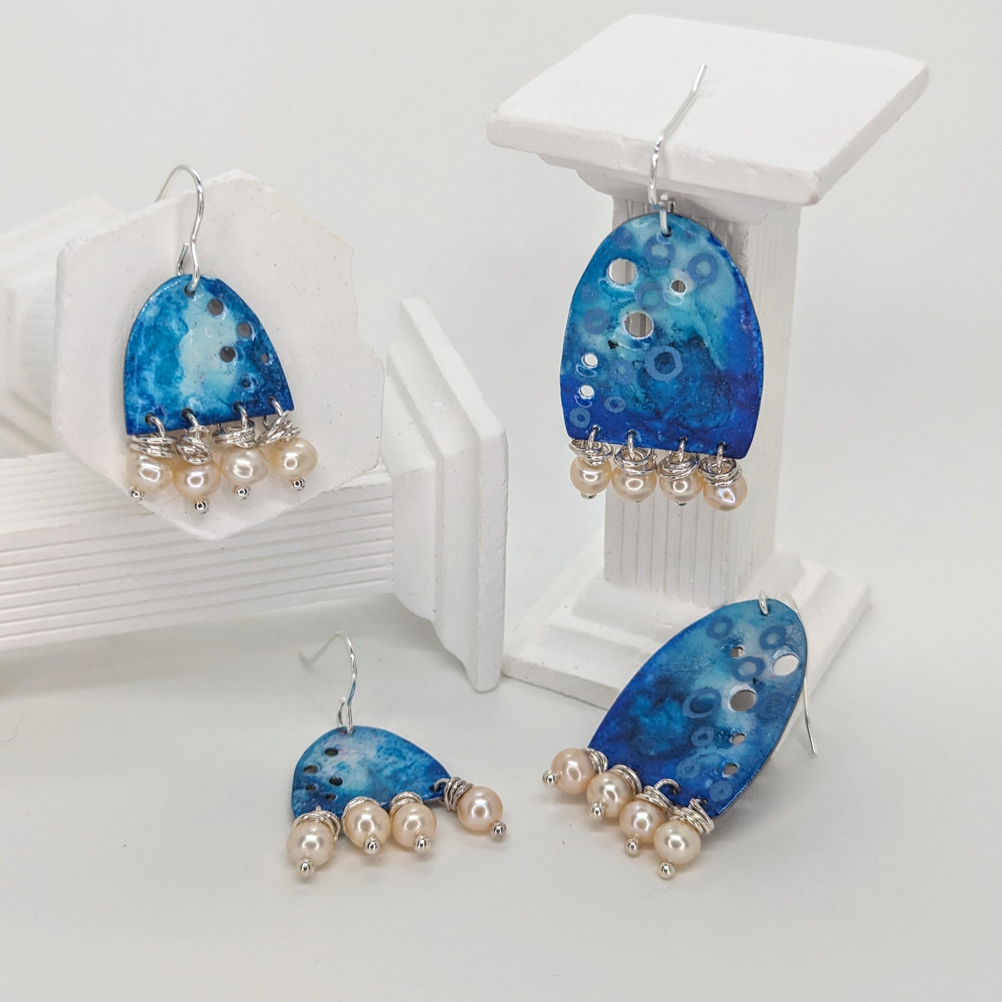 Calm blue Enamelled aluminium earrings with sterling silver earring hooks and adornments of freshwater pearls displayed on white columns 