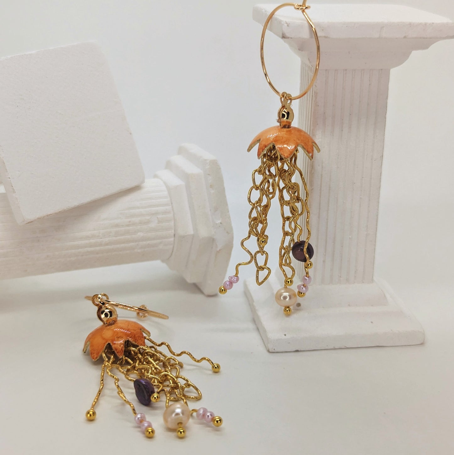 Orange Jelly fish inspired earrings with a cascade of gold plated tentacles with freshwater pearls. Displayed with shells 