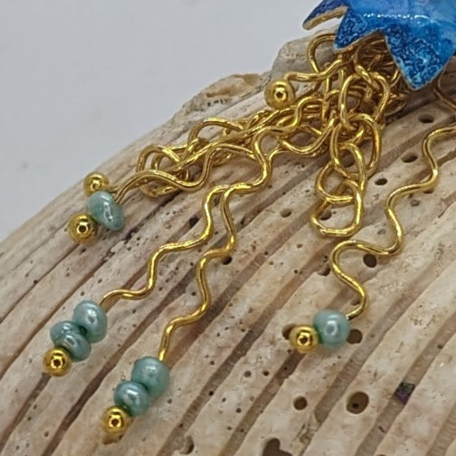 A close up of the jelly fish inspired earring's gold plated tentacles display on a close up of a sea shell. 